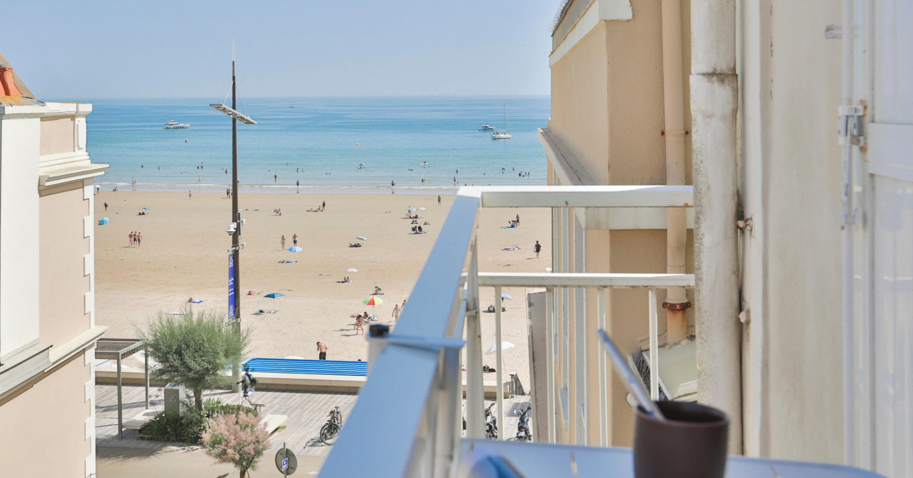 A beach view from a balcony with a clear sky, a sandy beach, and a few boats in the water.