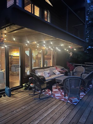 Una terraza con mobiliario exterior, un área de descanso cubierta y luces colgantes.