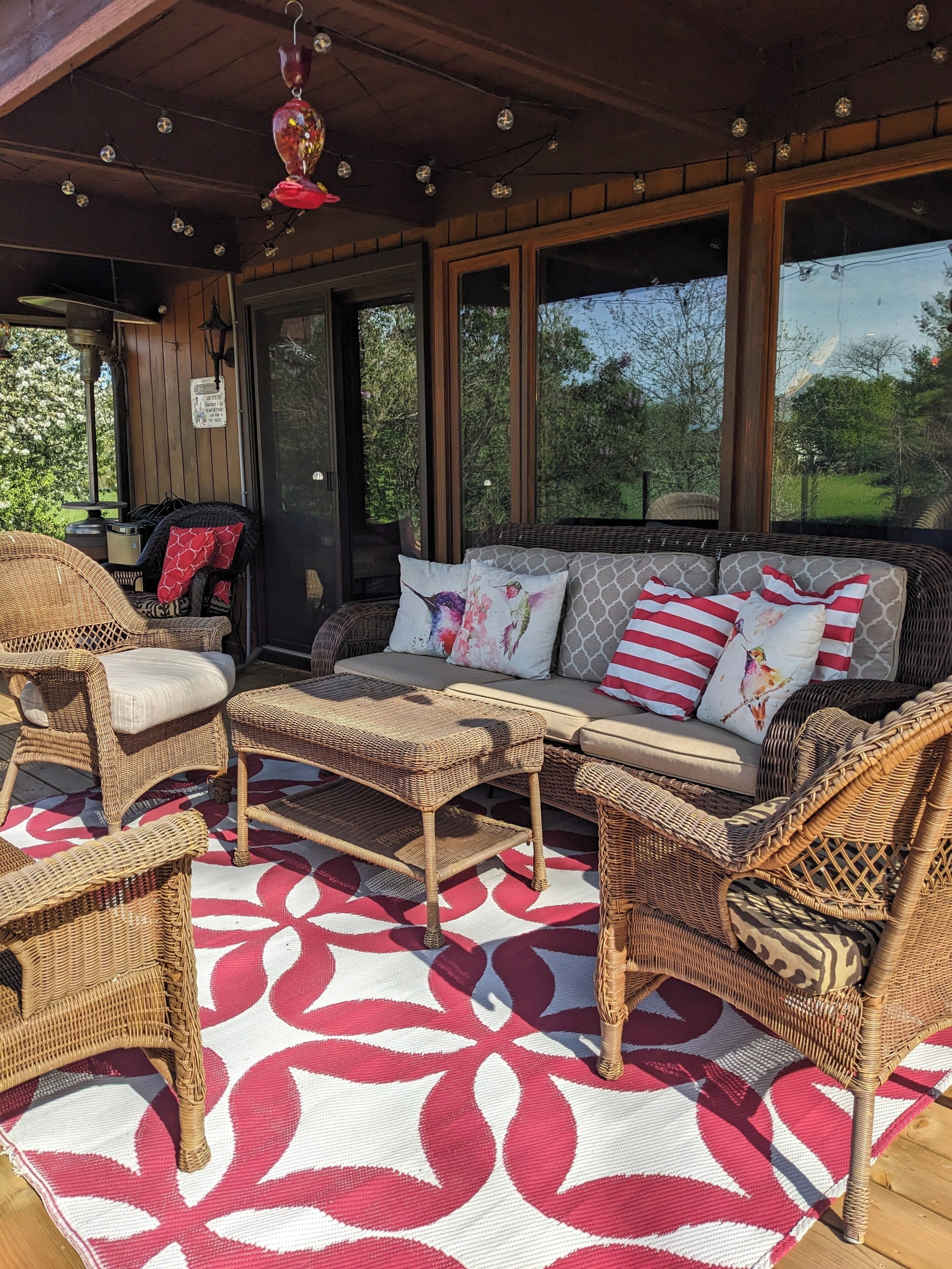 A covered outdoor seating area with wicker furniture, a patterned rug, and large windows.