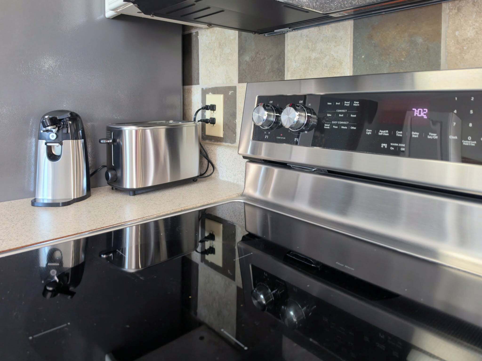 A modern kitchen with stainless steel appliances, including a toaster, a kettle, and an oven with a digital control panel.
