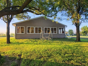 A two-story house with a porch, surrounded by grass and trees.