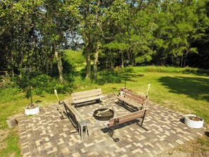 An outdoor seating area with a fire pit, benches, and a paved ground.