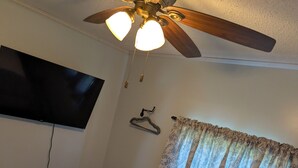 A hotel room with a bed, a ceiling fan, a TV mounted on the wall, and a window with patterned curtains.