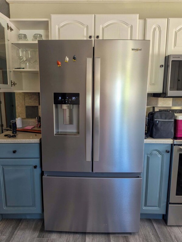 A stainless steel refrigerator with a water dispenser and a digital display, set in a kitchen with light blue cabinets and a tiled backsplash.