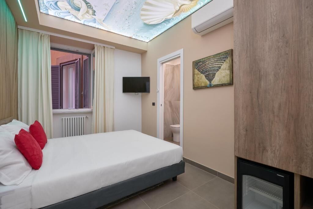 Un dormitorio con una cama, televisión, techo con lámpara, puerta y un refrigerador pequeño.