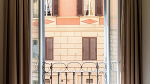 A hotel room with a balcony, a bed with a neatly folded blanket, and a view of the building's facade.