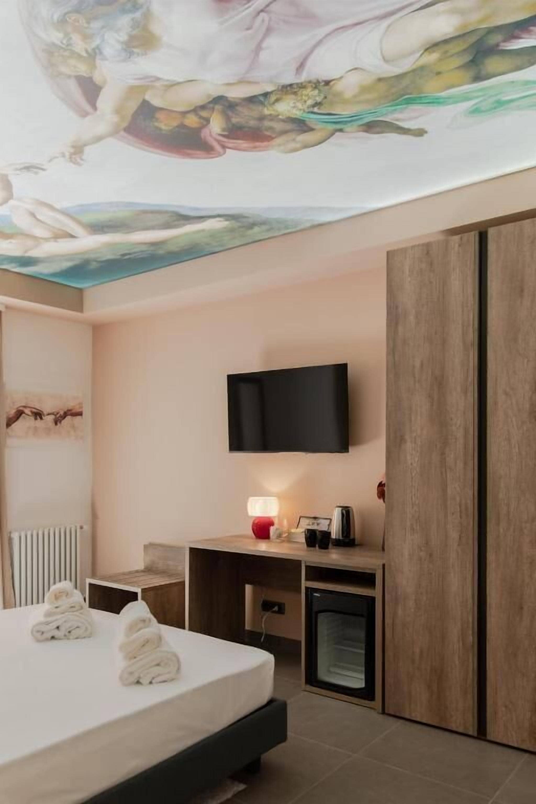 Habitación de hotel con cama, escritorio, televisor, armario y un mural en el techo.