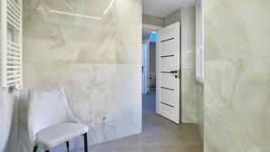 A hallway with a white chair, marble walls, and a door leading to another room.