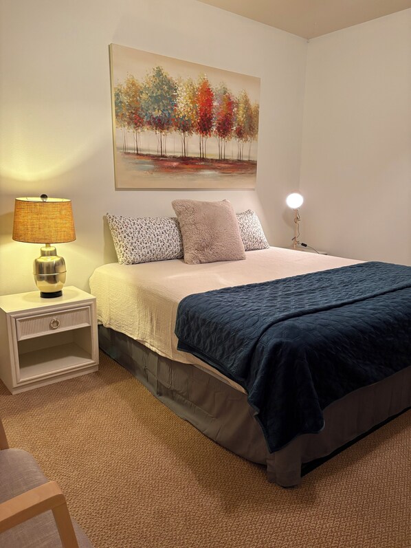 A bedroom with a bed, nightstand, lamp, and a painting on the wall.