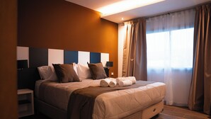 Quarto de hotel moderno com uma cama grande, uma mesa de cabeceira, um abajur e uma janela com cortinas.