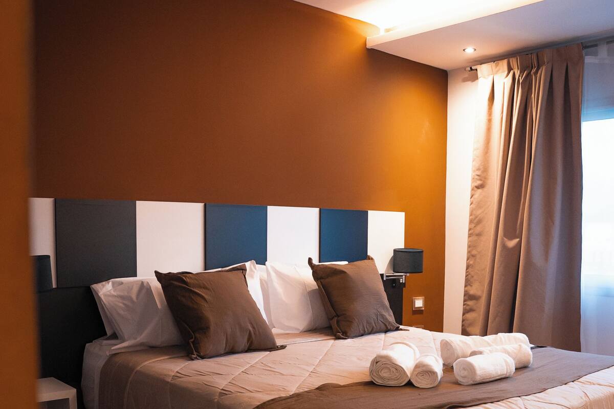 A neatly made bed with pillows, a bedside lamp, and rolled towels.