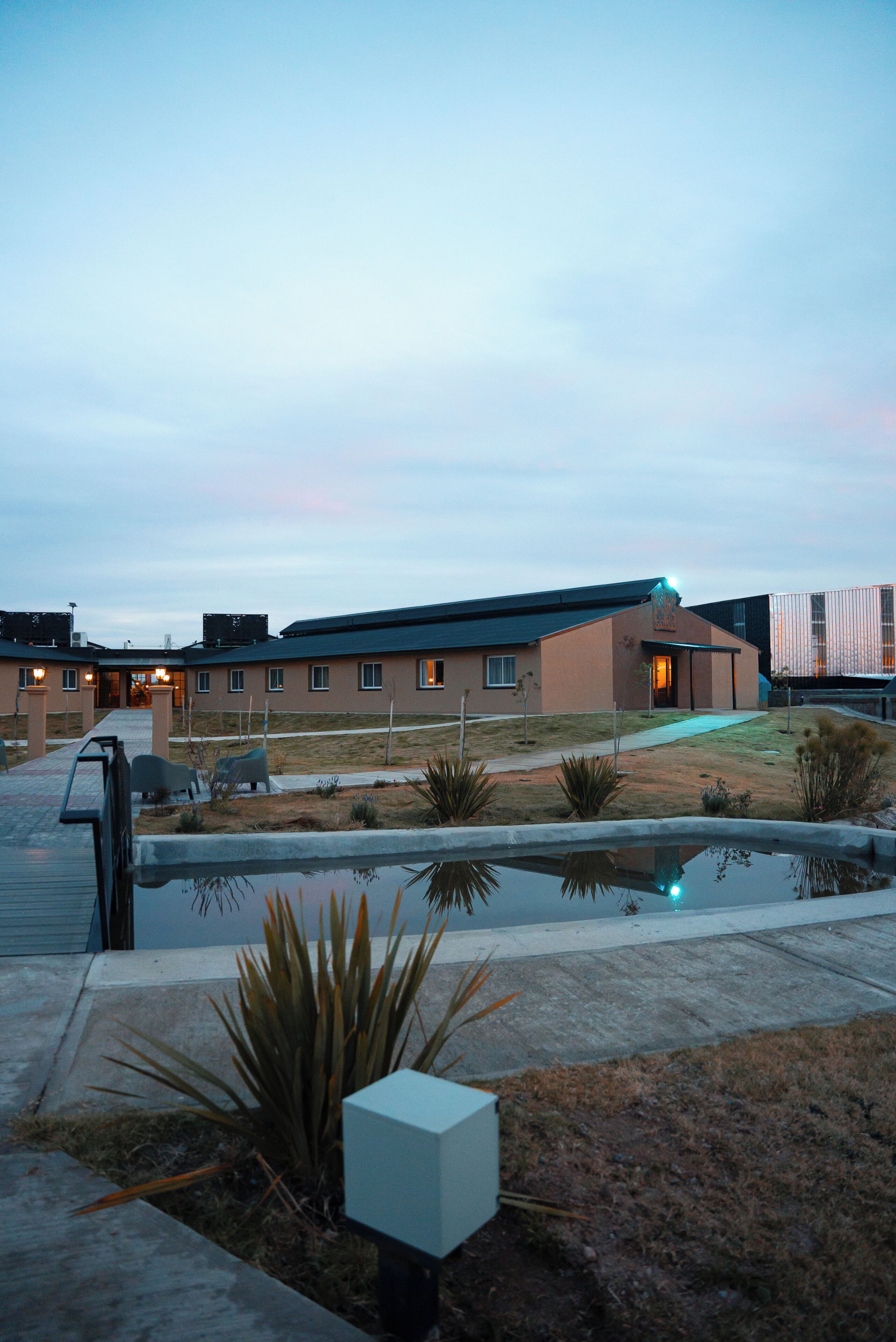 A building with a flat roof, a paved entrance, and a small pond in the foreground.