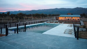 Uma piscina com espreguiçadeiras, uma área cercada e um edifício com telhado verde.