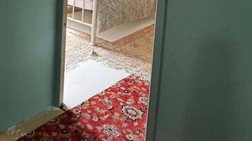 A bedroom with a bed, a wooden headboard, a red patterned rug, and a floral wreath on the wall.