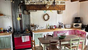 Una cocina rústica con una mesa de madera, sillas y una estufa roja.