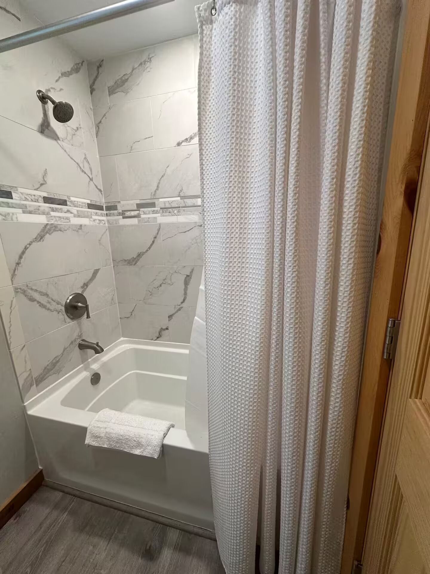 A shower with a marble wall, a bathtub, and a white shower curtain.