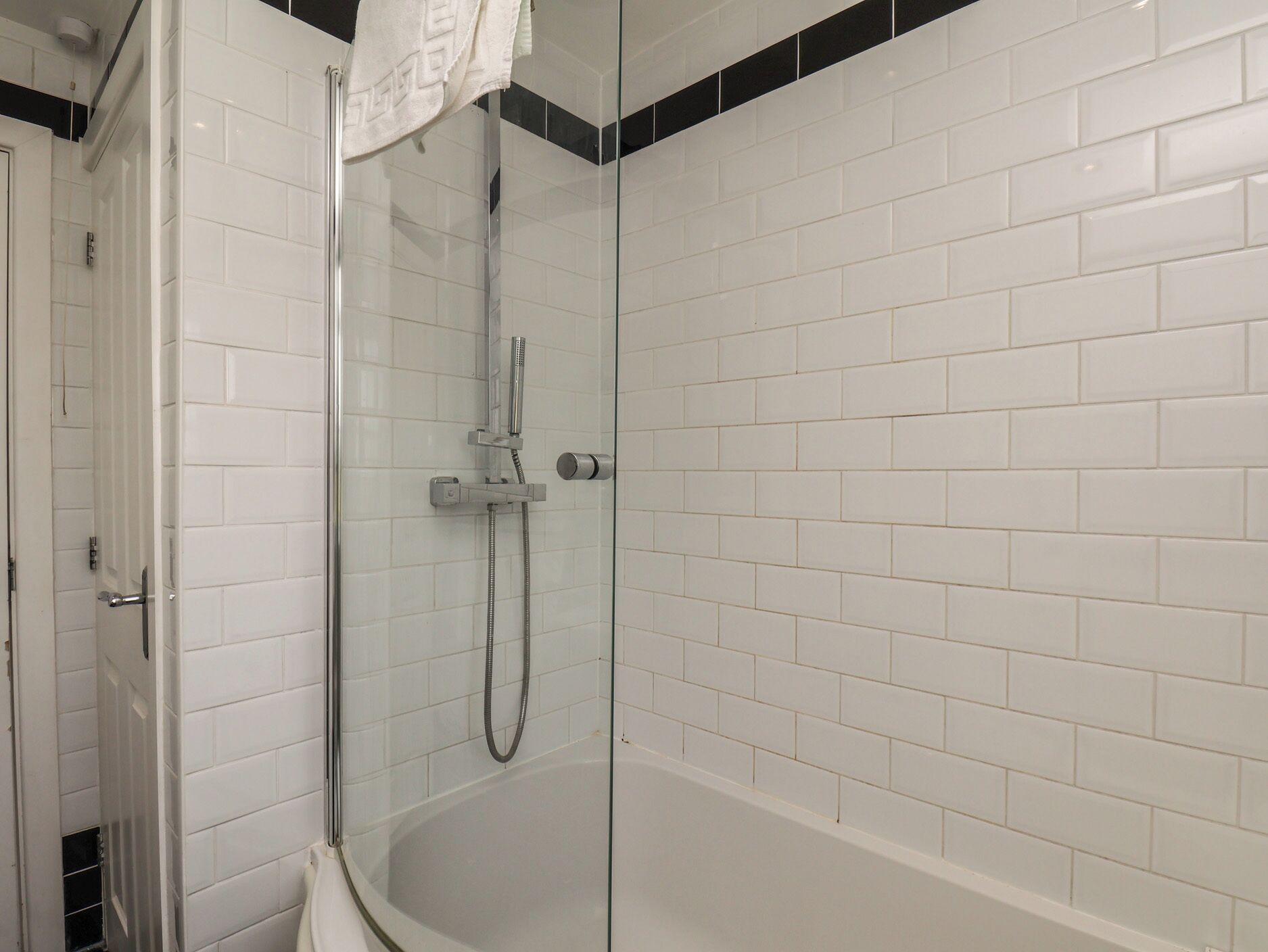A glass-enclosed shower with a handheld showerhead and a handheld hose, white tiled walls, and a visible door.