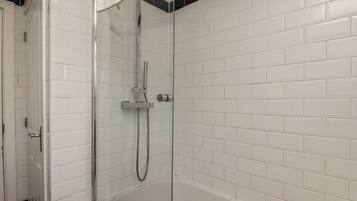 A glass-enclosed shower with a handheld showerhead and a handheld hose, white tiled walls, and a visible door.