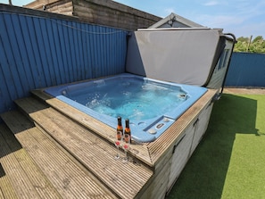 A hot tub with steps leading up to it, surrounded by a blue fence and a wooden deck. - Overcarr Cottage (Malton)