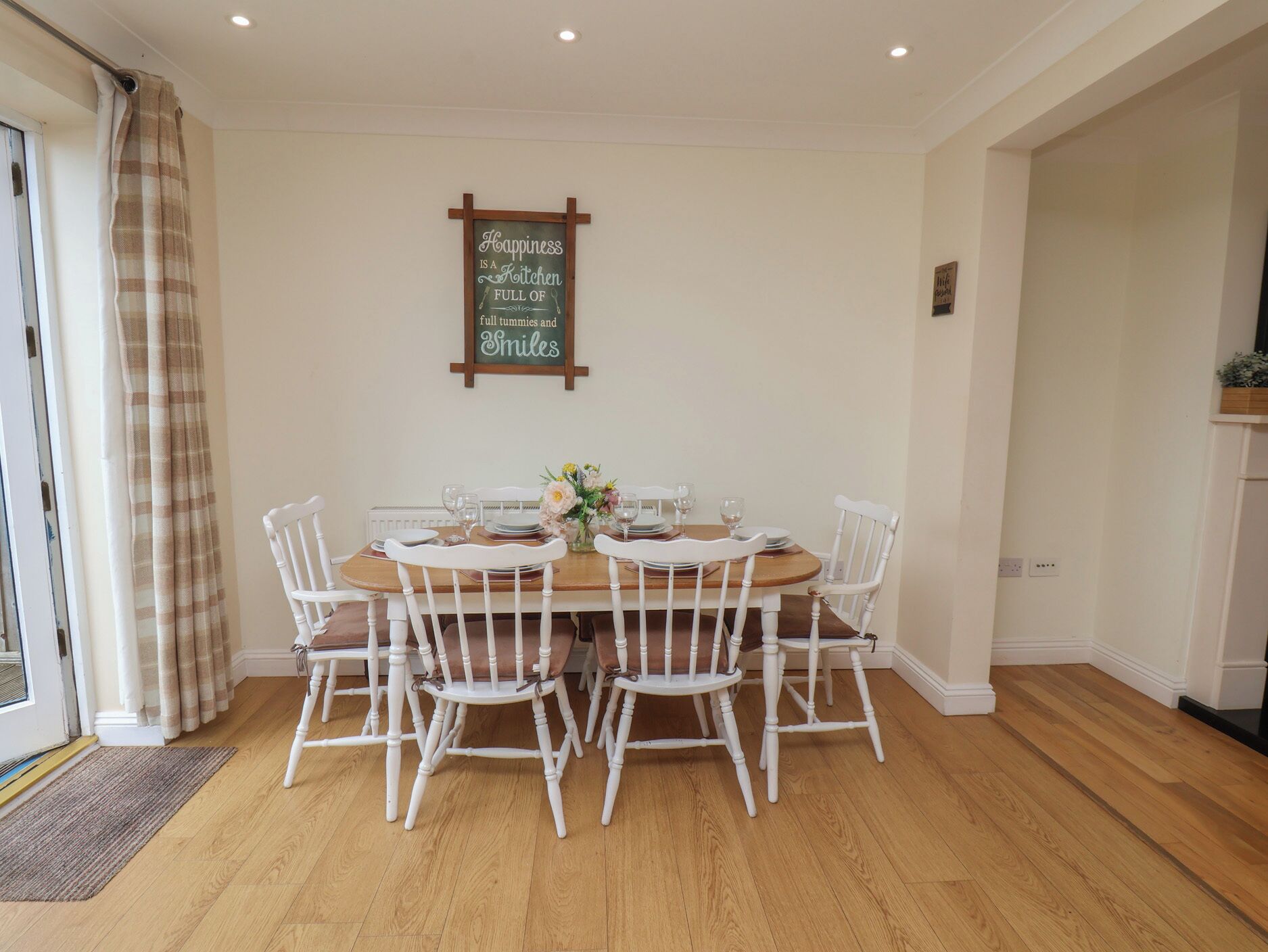 A dining area with a wooden table, white chairs, and a sign on the wall.