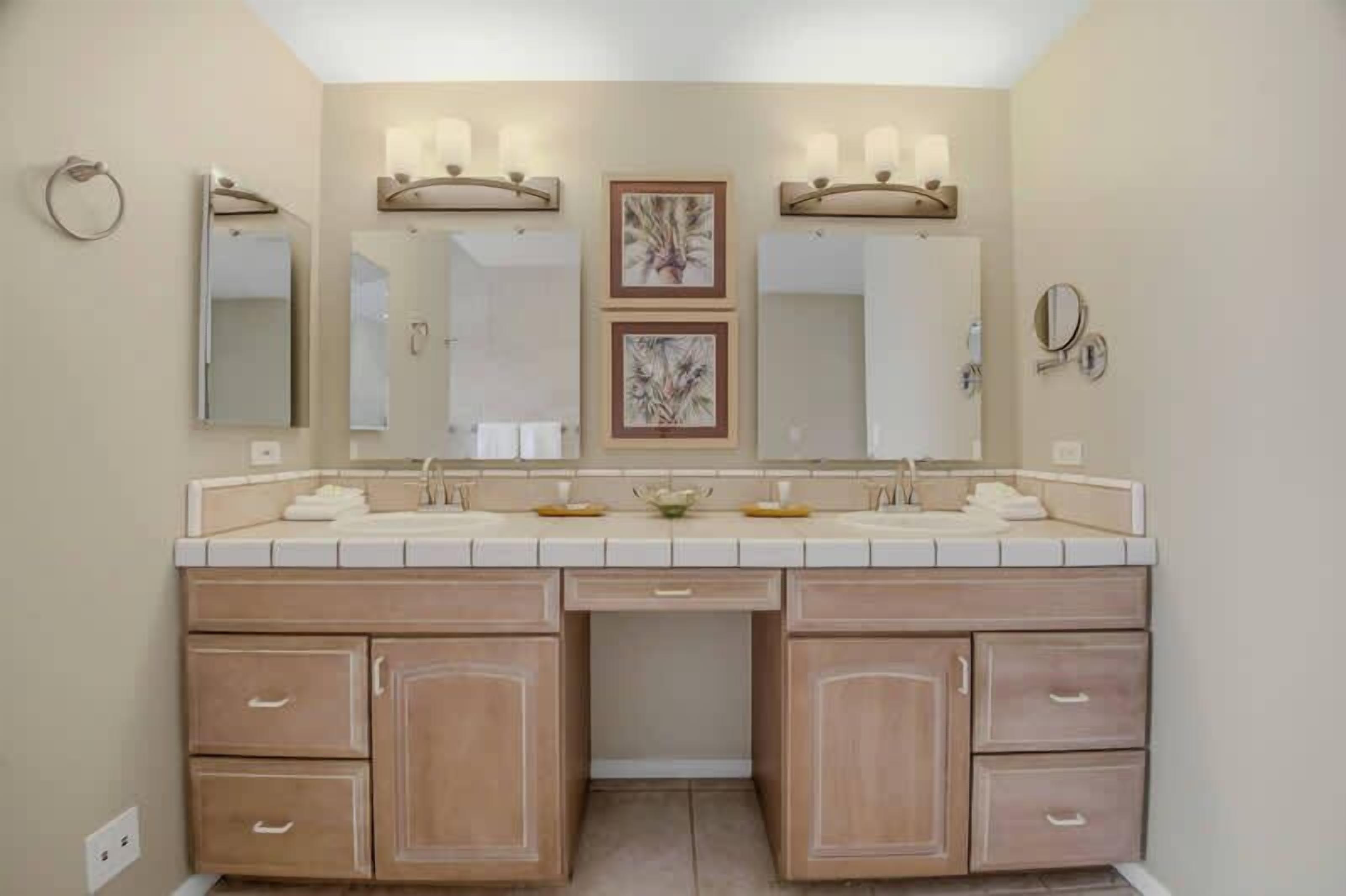 A bathroom with a double vanity, two mirrors, a towel rack, and a framed picture on the wall.
