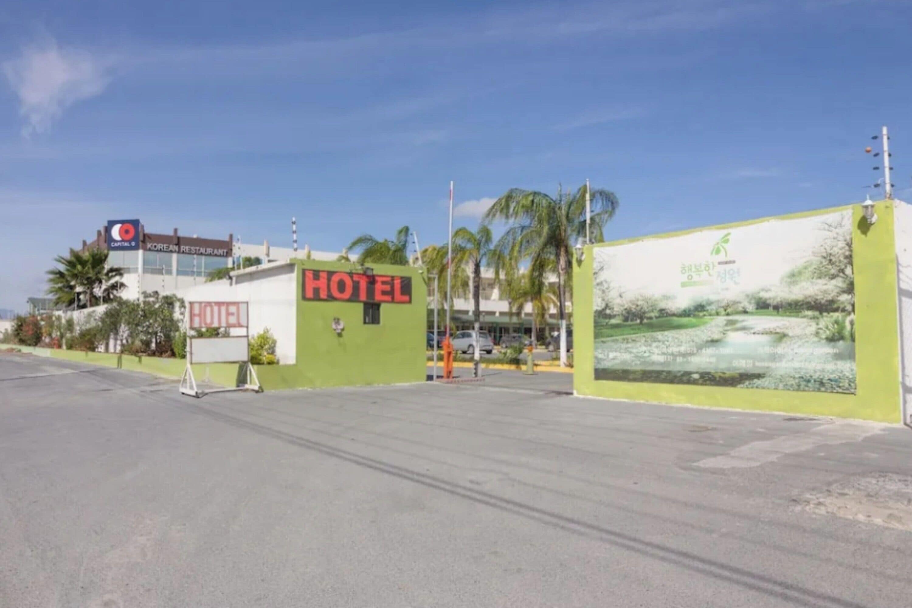 A hotel with a prominent 'HOTEL' sign, a Korean restaurant sign, and a large billboard with a landscape image.