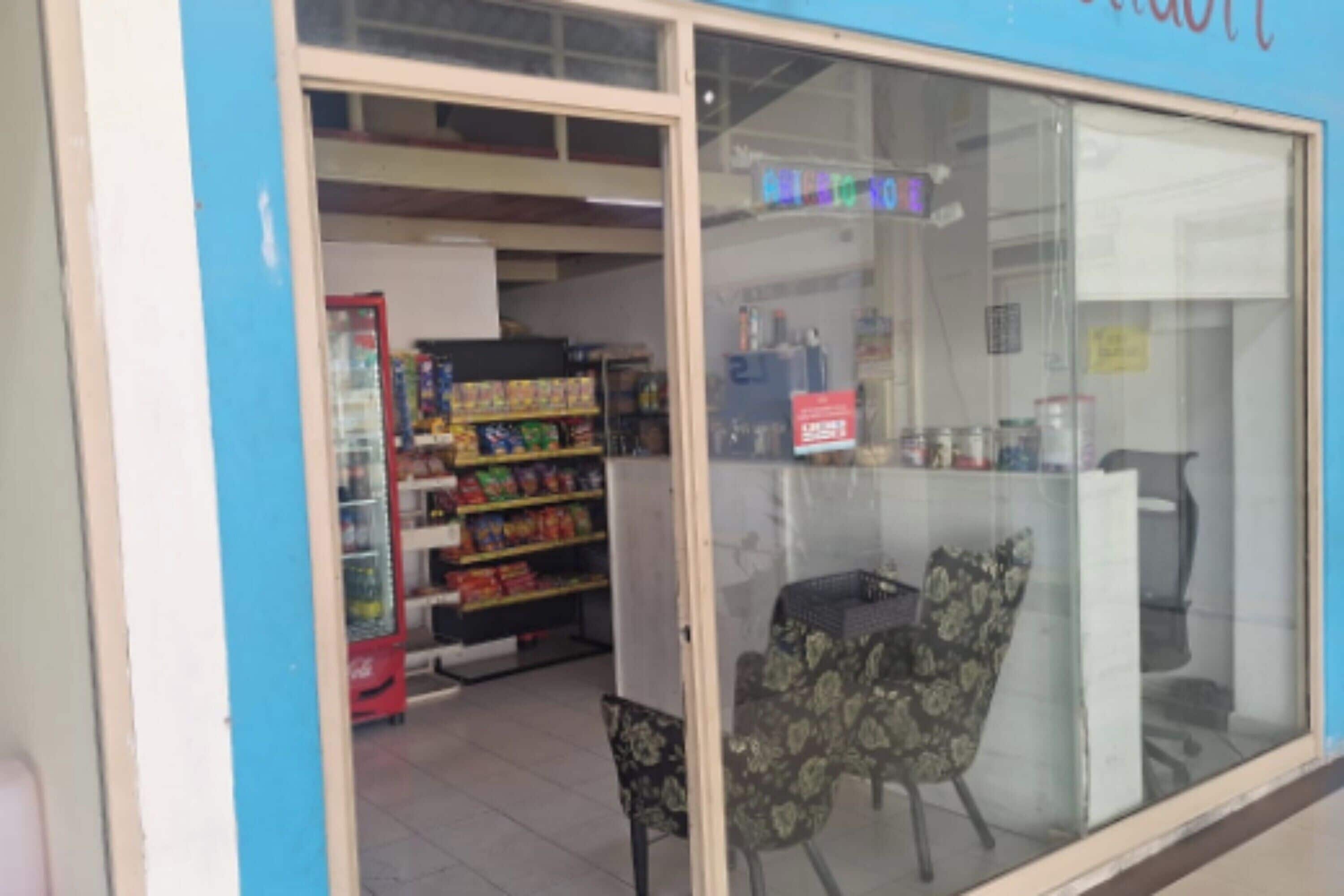 A storefront with a glass door, shelves stocked with various products, and a chair outside.