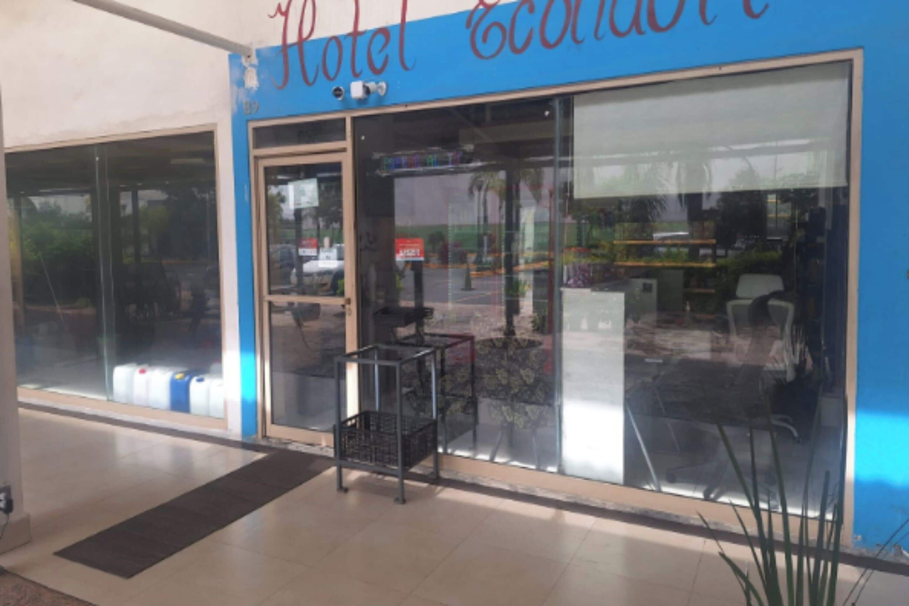 A hotel entrance with a blue sign, large glass windows, and a small outdoor seating area.