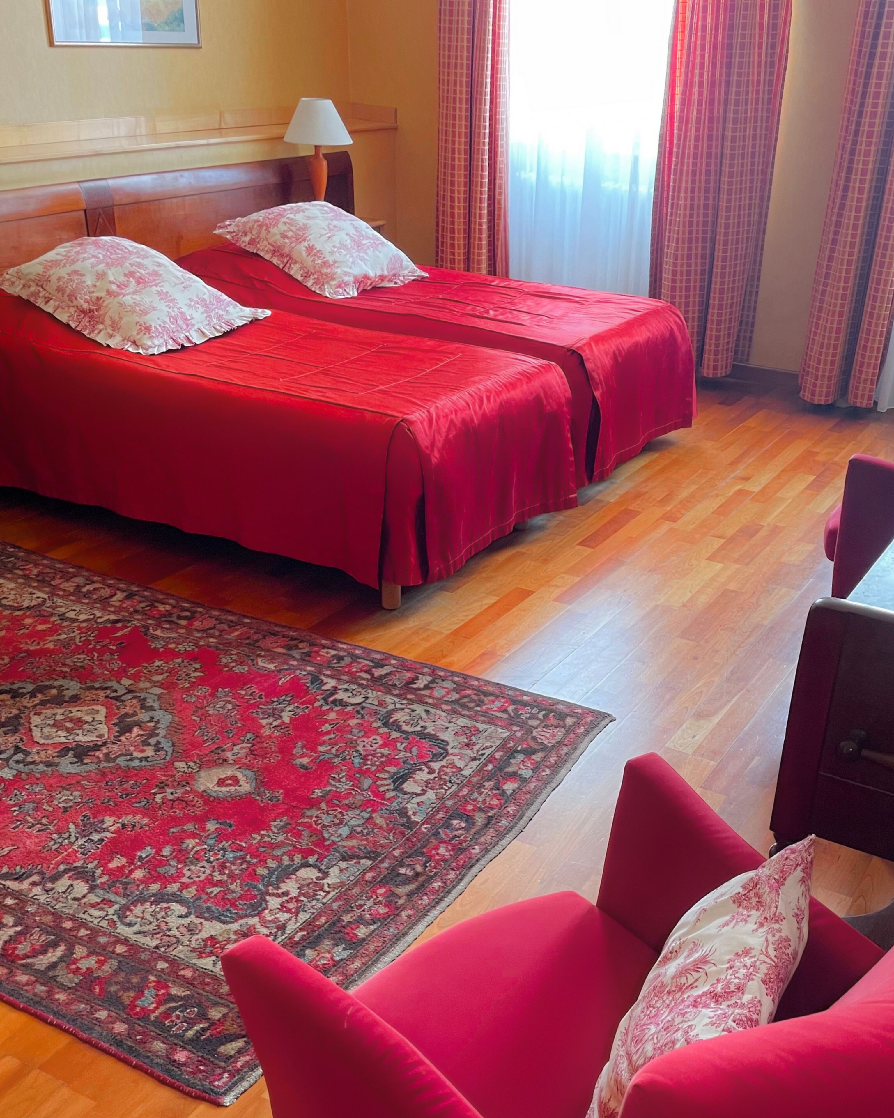 A hotel room with two beds, a red carpet, and a red chair.