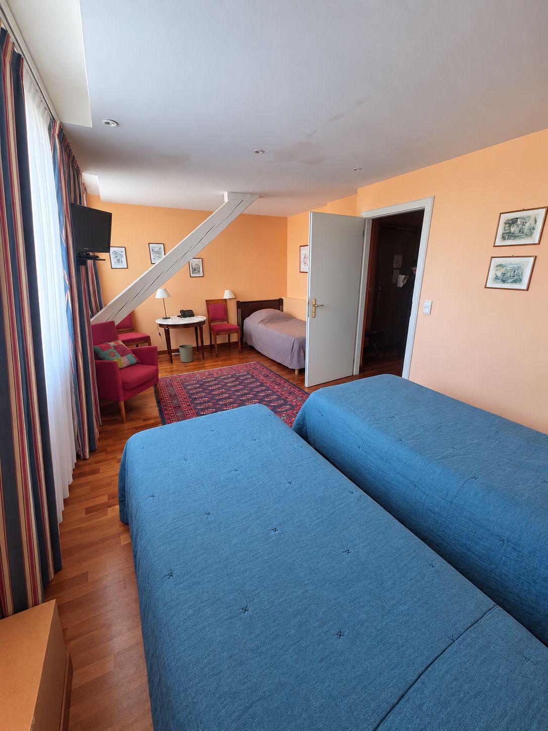 Een kamer met twee bedden, een bureau, een stoel, een televisie en een trap.