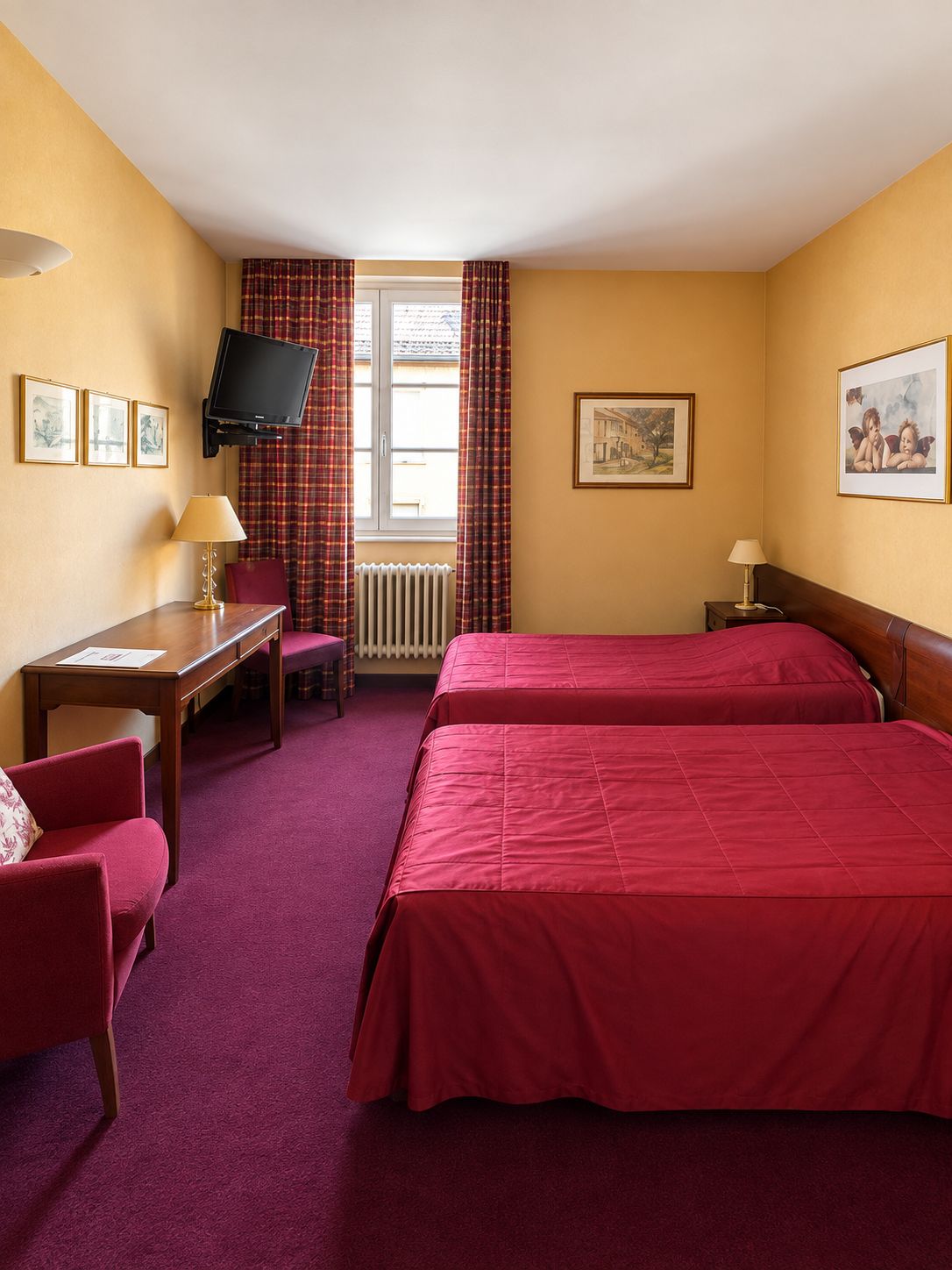 A hotel room with two beds, a desk, a chair, a television, and a window with curtains.