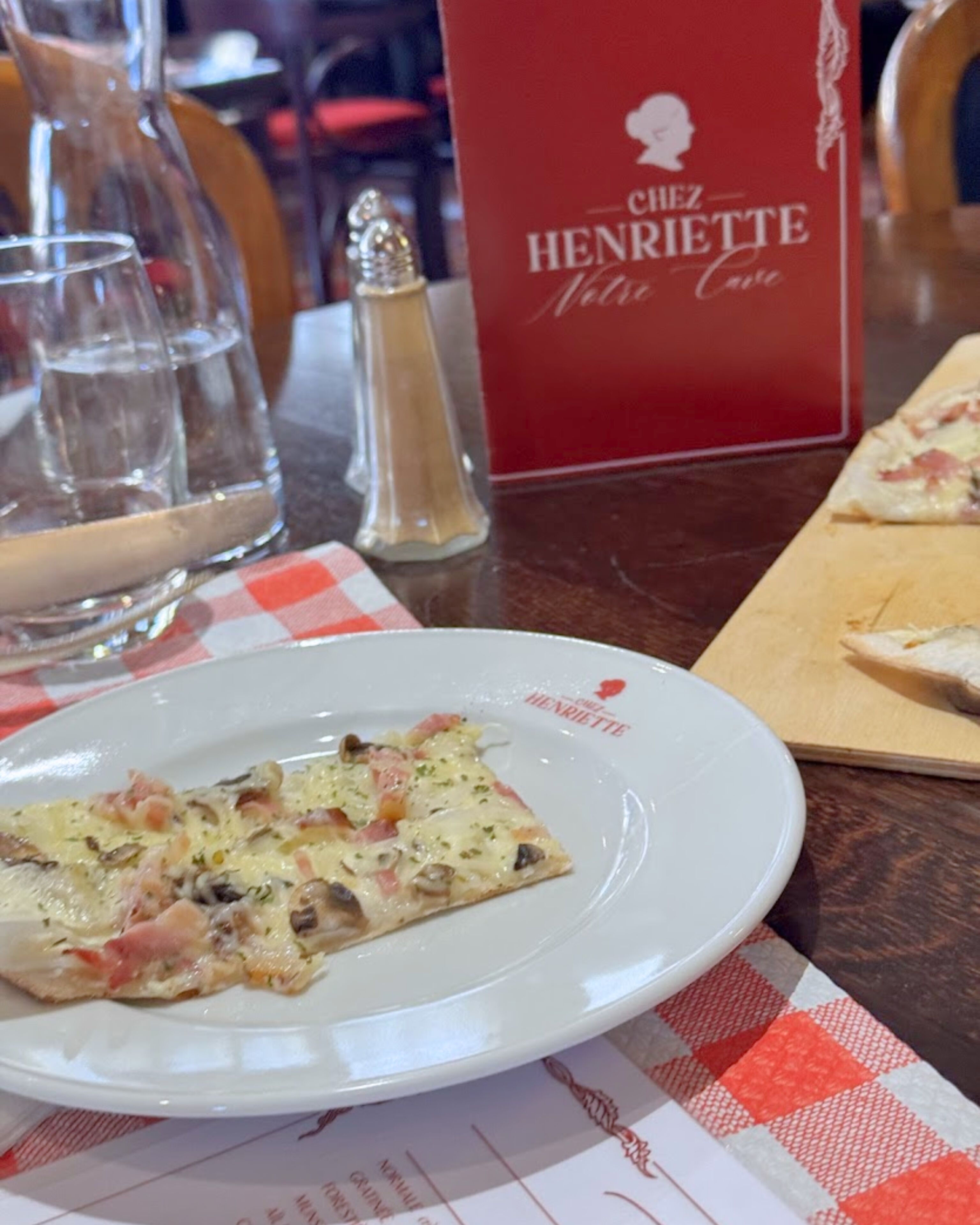 Un plato con una porción de pizza sobre una mesa con un menú rojo y saleros y pimenteros.