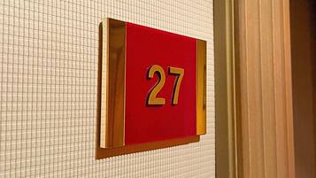Een close-up van een hotelkamer nummerbordje, '27', bevestigd aan een betegelde muur.