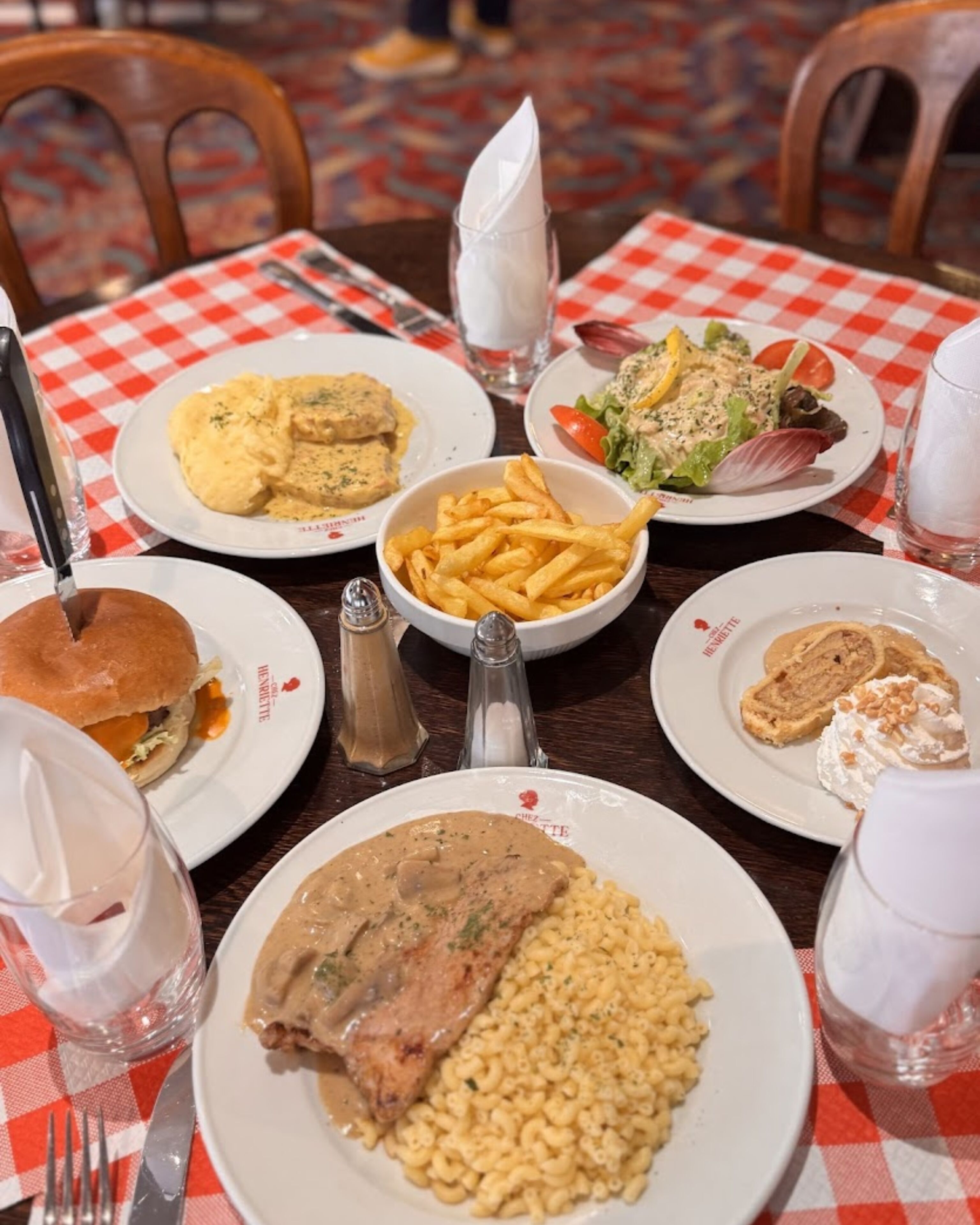 Ein Tisch mit verschiedenen Gerichten, darunter ein Steak, Makkaroni und Salat, bedeckt mit einer rot-weißen Karotischdecke.
