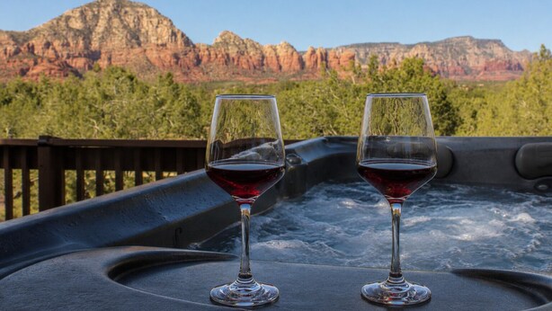 Dos copas de vino tinto en un jacuzzi con un paisaje montañoso al fondo.