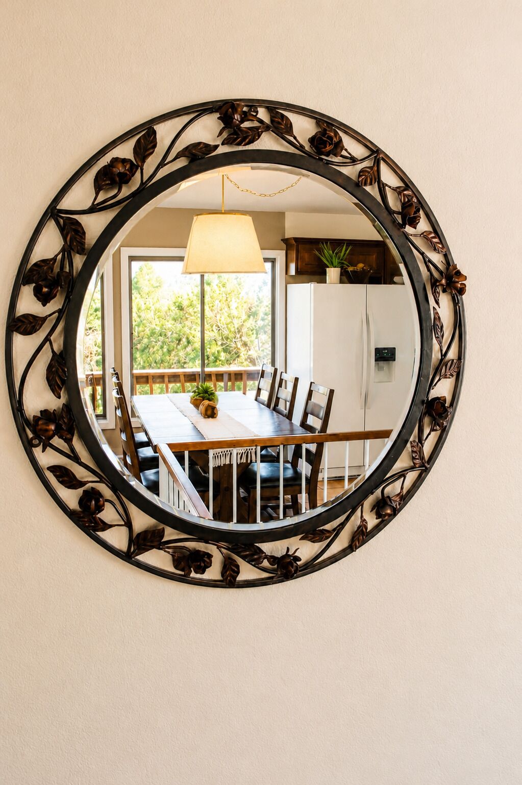 Un miroir rond avec un cadre en métal orné de motifs floraux, accroché au mur.