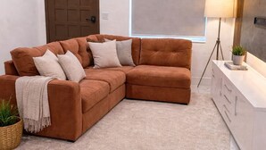 A modern living room with a sectional sofa, a standing lamp, a potted plant, and a large window. - 5640 NE Miami (Miami)
