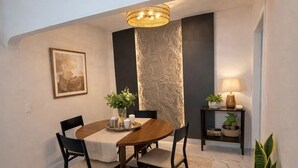 A dining area with a marble floor, a wooden table, black chairs, a textured wall, a hanging light fixture, a small table with a lamp, and a potted plant. - 5640 NE Miami (Miami)