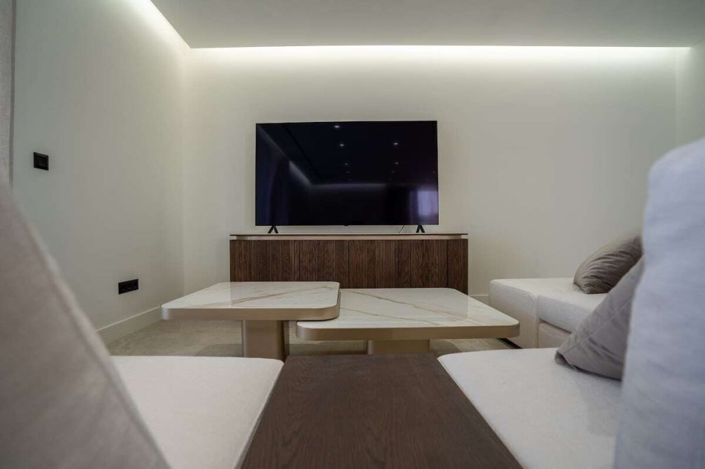 A modern living room with a flat-screen TV mounted on a wooden panel, two white sofas, and a small table.