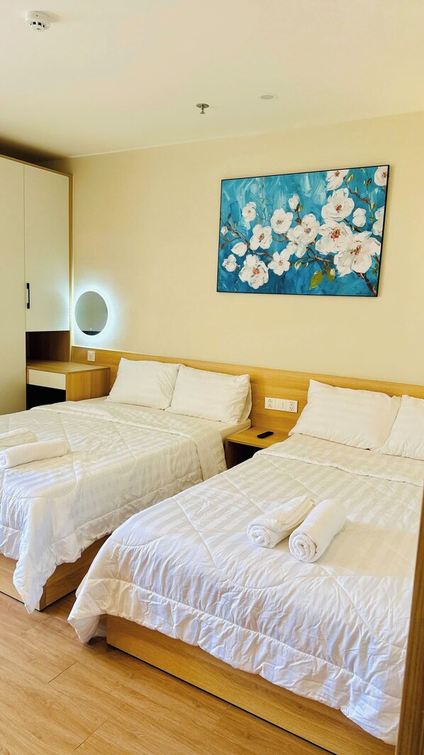 A hotel room with two beds, a painting of flowers, a round mirror, and a wooden headboard. - Zansea Home & Apartment (Da Nang Municipality)