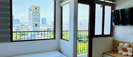 A modern bedroom with a large bed, a TV mounted on the wall, and a balcony with a city view.