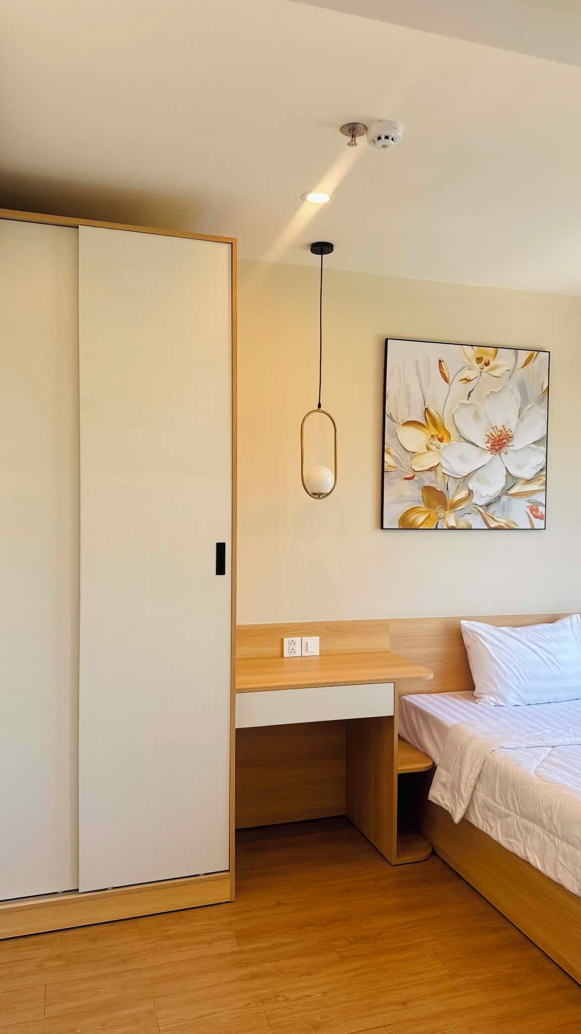 A bedroom with a bed, a desk, a wardrobe, and a ceiling-mounted light fixture.