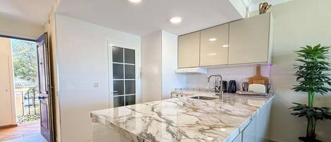 A modern kitchen with a marble countertop, built-in cabinets, and a window.