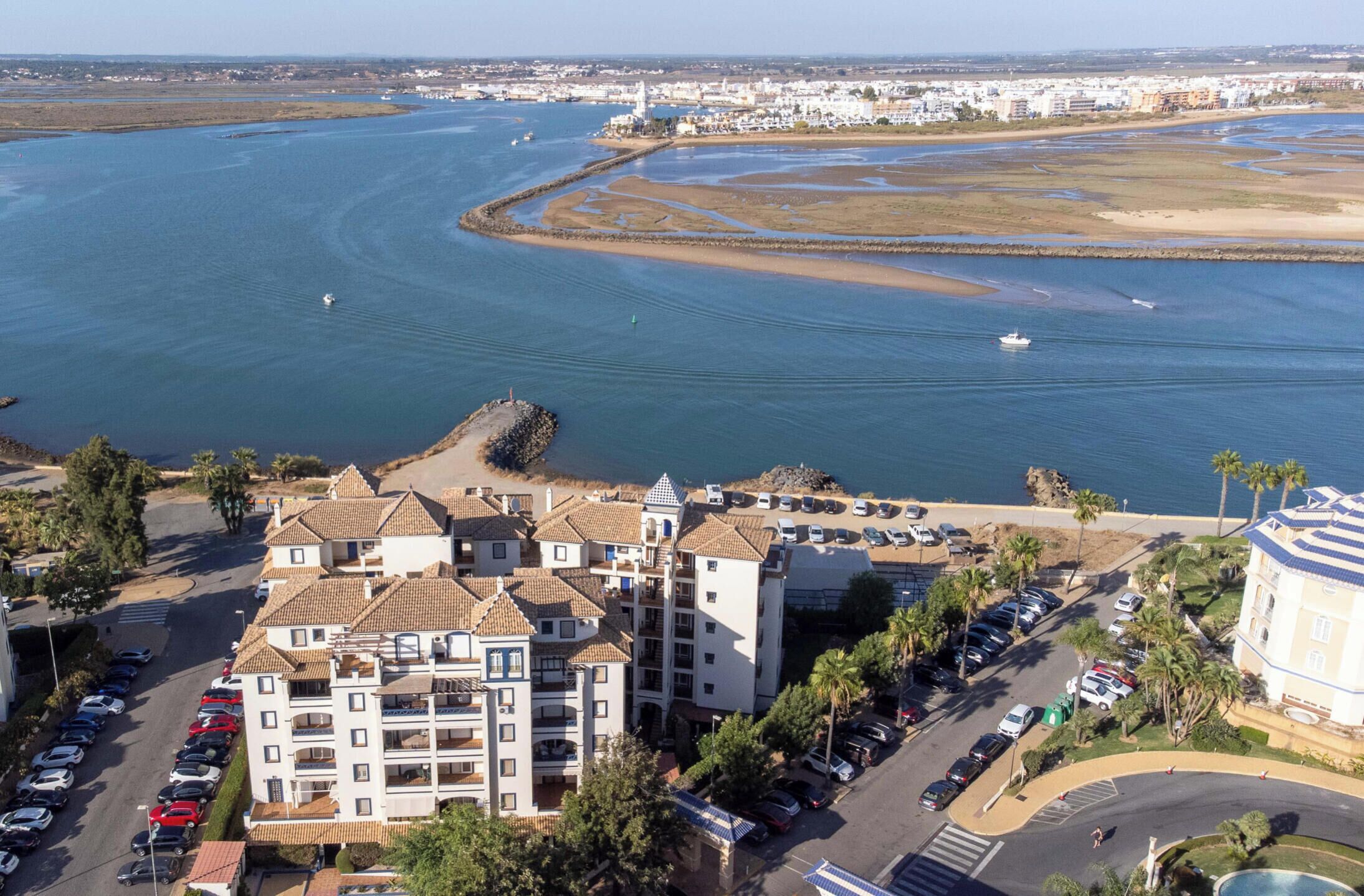 A coastal hotel with multiple floors, a parking lot, and a view of the sea.