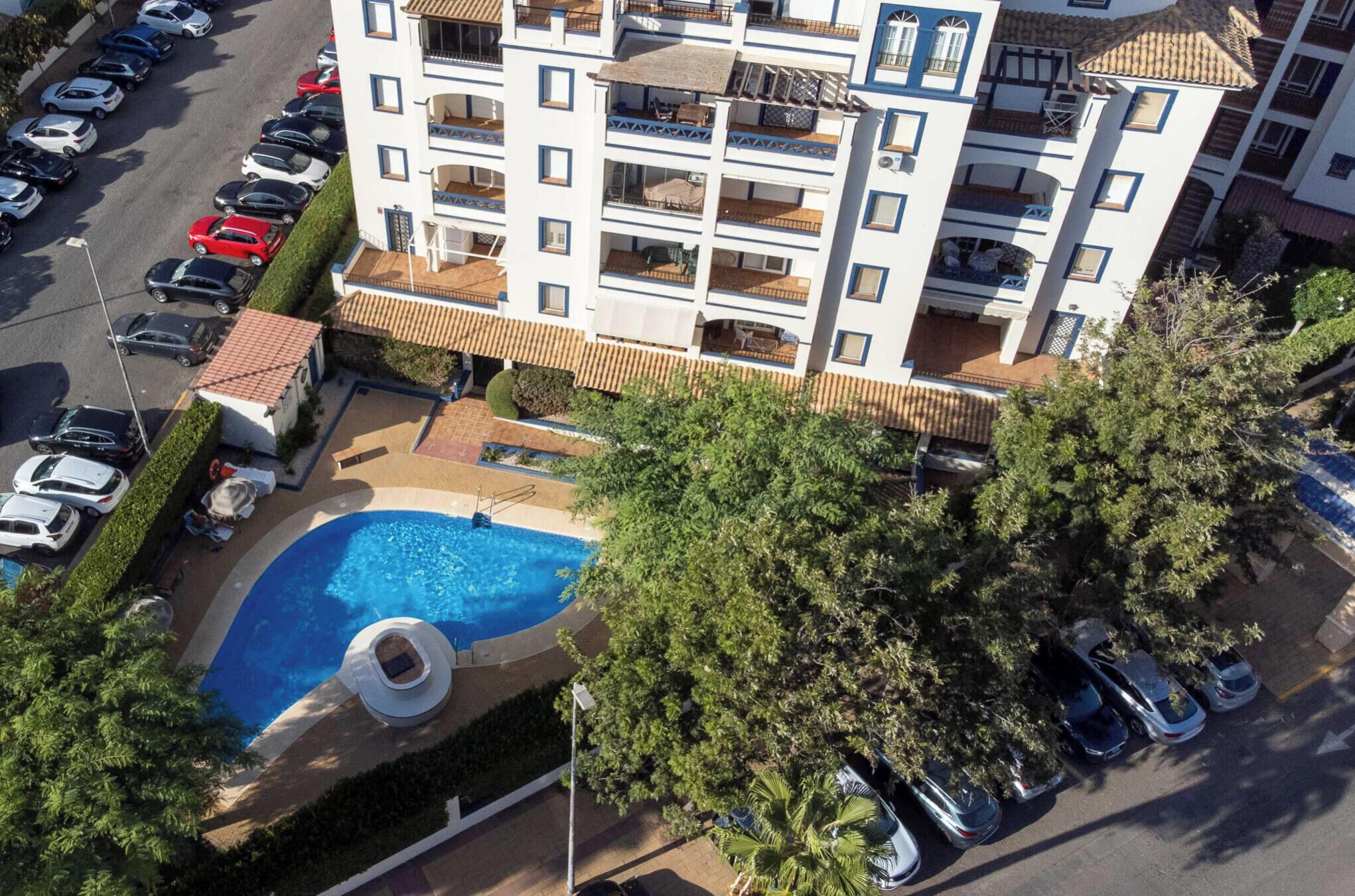 A multi-story hotel with a swimming pool, balconies, and parked cars.