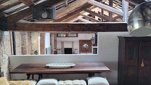 Un intérieur rustique avec des poutres apparentes, un banc en bois agrémenté de coussins, un tapis à motifs et un grand miroir décoratif.