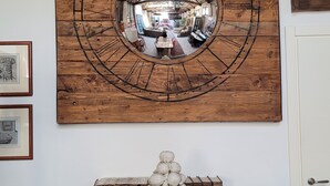 Une horloge murale en bois avec un miroir rond, une table avec des livres, une machine à écrire et un bol décoratif.