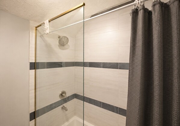 A shower with a glass door, a handheld showerhead, and a towel rack.