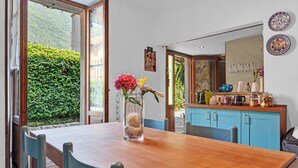 Un coin repas avec une table en bois, des chaises, un vase de fleurs, et un espace cuisine avec des placards et un plan de travail.