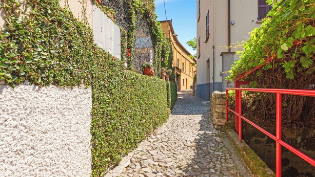 Une ruelle étroite pavée, bordée d’un côté par un mur de pierre et de l’autre par une rambarde métallique rouge.